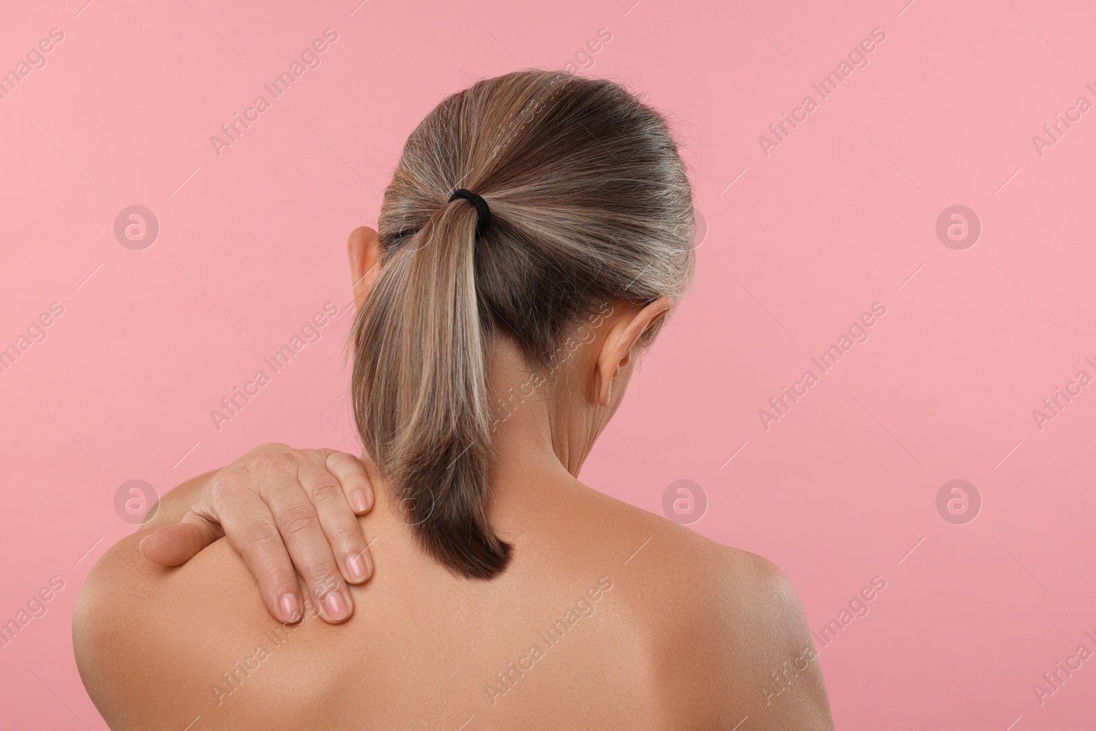 Photo of Woman suffering from pain in her neck on pink background, back view