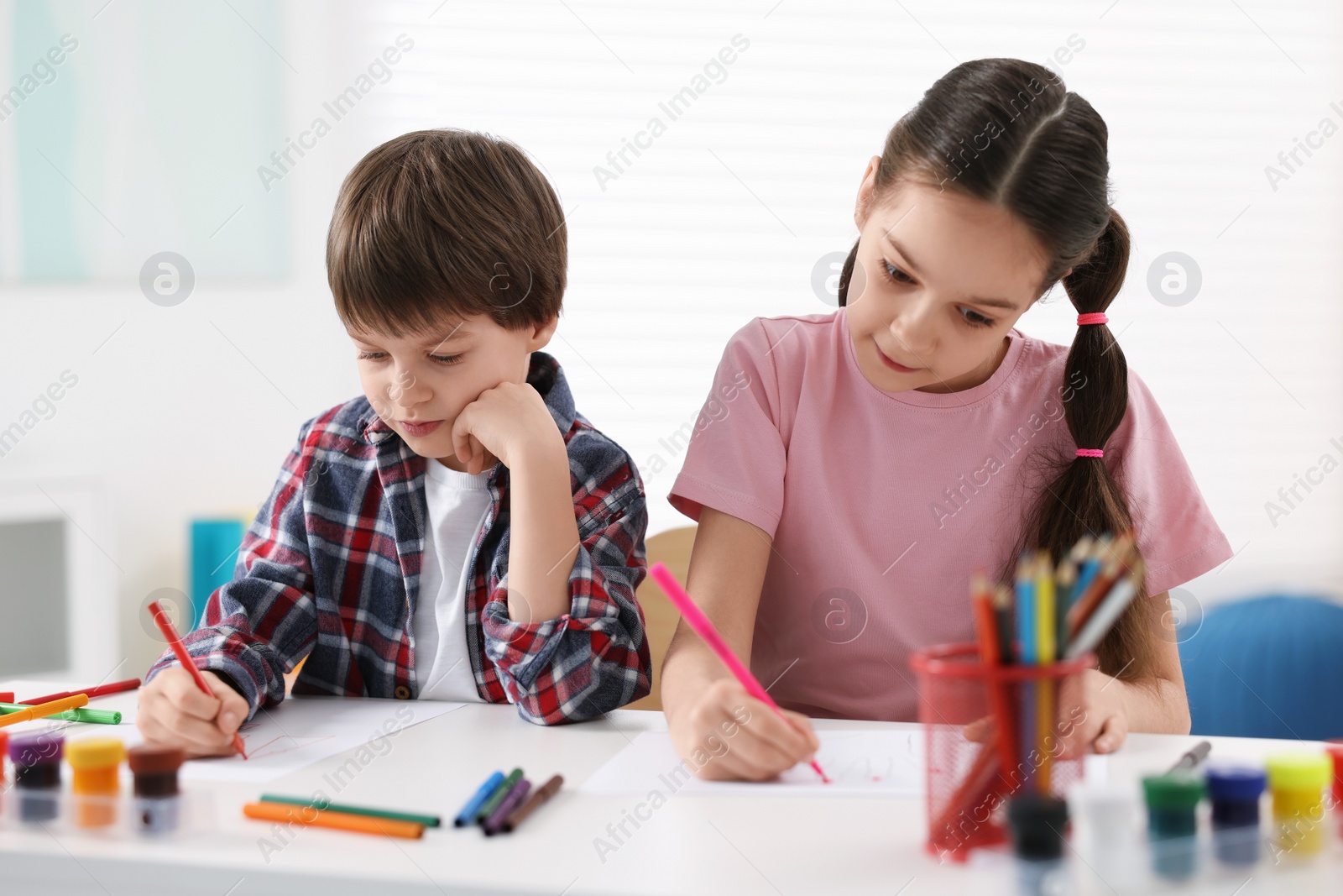 Photo of Happy brother and sister drawing at white table in room