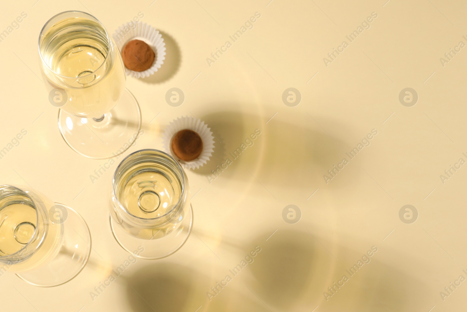 Photo of Glasses of delicious sparkling wine and chocolate truffles on light yellow background, above view. Space for text