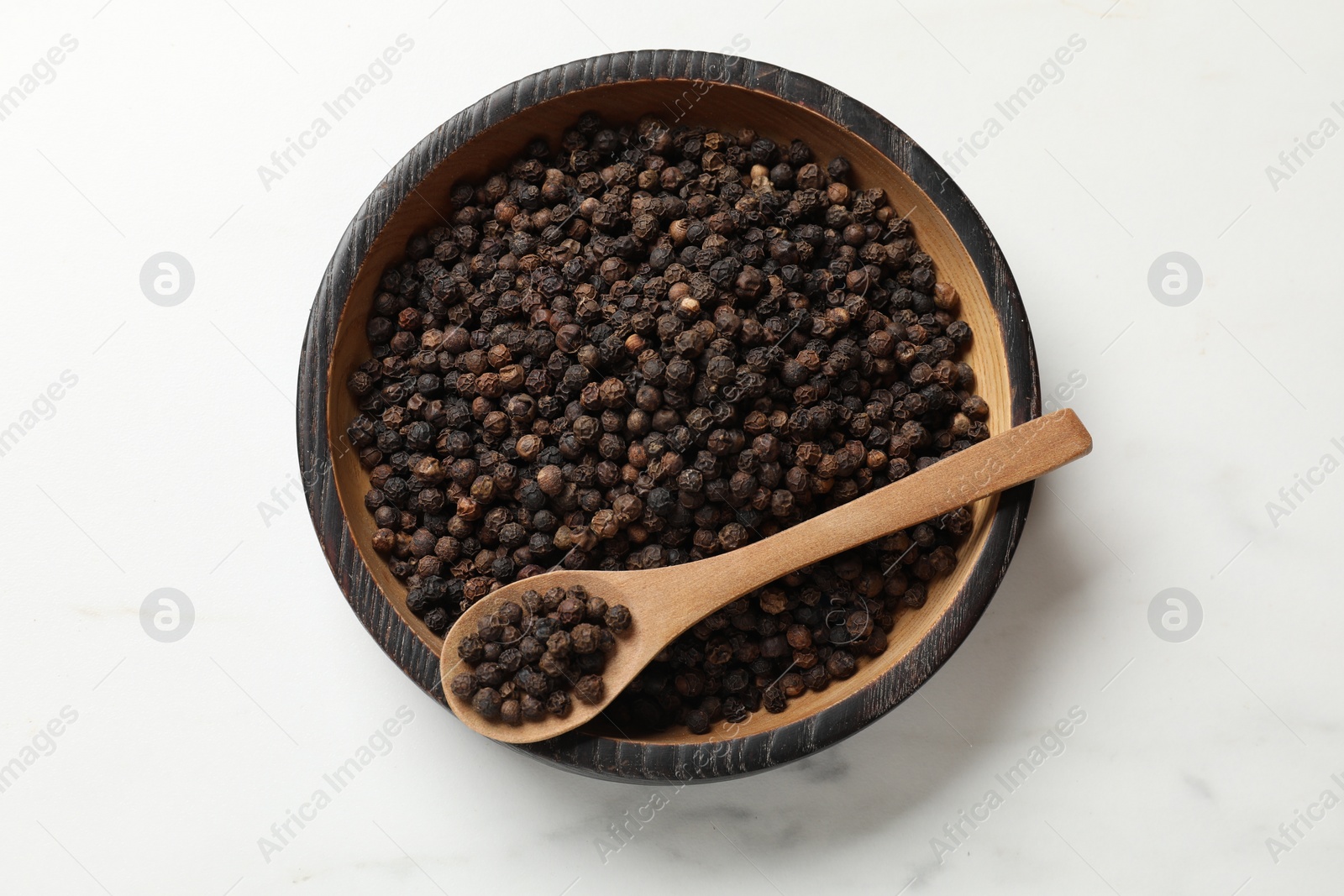 Photo of Aromatic spice. Black pepper in bowl and spoon on white table, top view