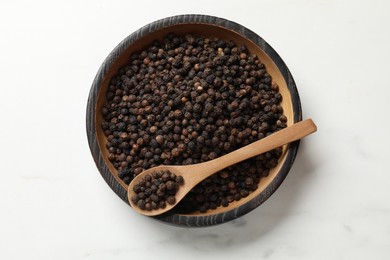 Aromatic spice. Black pepper in bowl and spoon on white table, top view