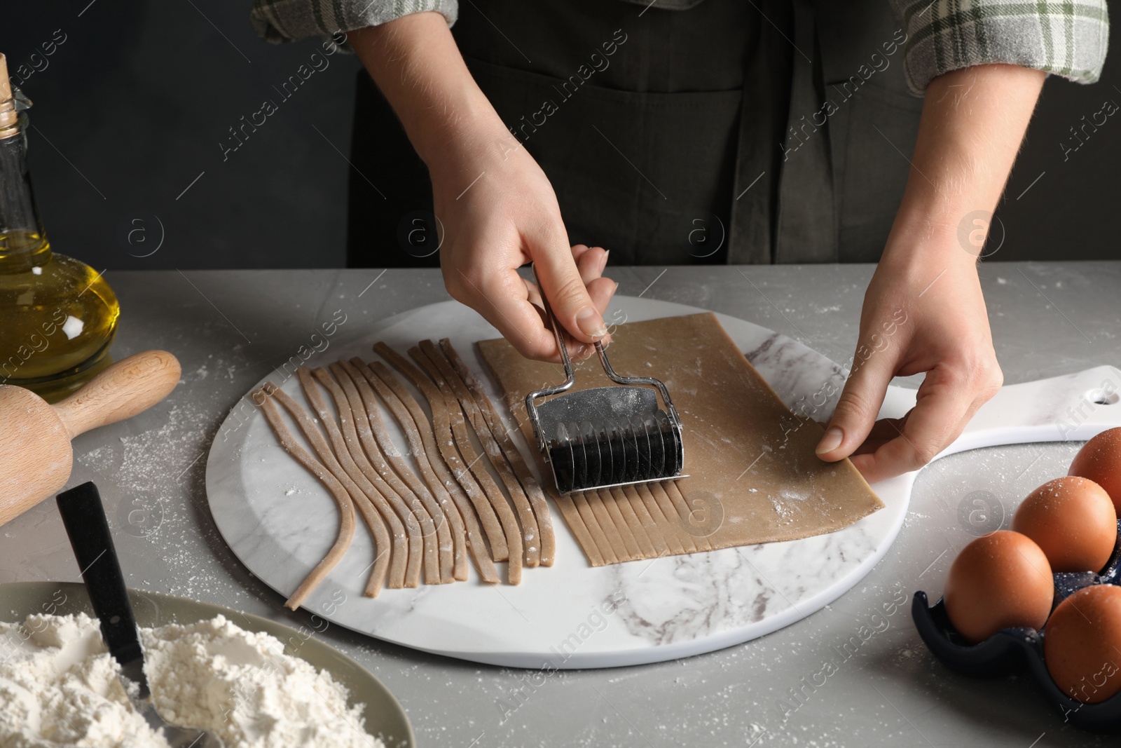 Photo of Woman making soba (buckwheat noodles) with cutter at grey table, closeup