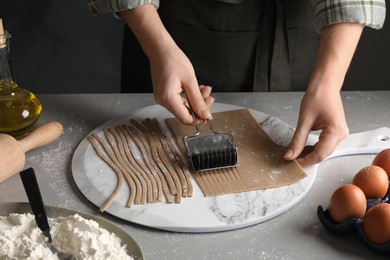 Woman making soba (buckwheat noodles) with cutter at grey table, closeup