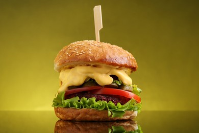 Photo of Delicious vegetarian burger on mirror surface against olive background