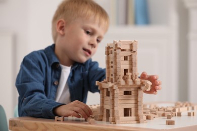 Photo of Cute little boy playing with wooden tower at table indoors, selective focus. Child's toy