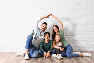 Photo of Happy family forming roof with their hands near brick wall. Insurance concept