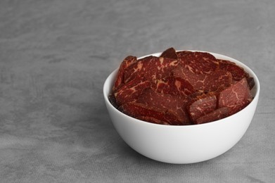 Photo of Delicious beef jerky in bowl on light gray table, space for text