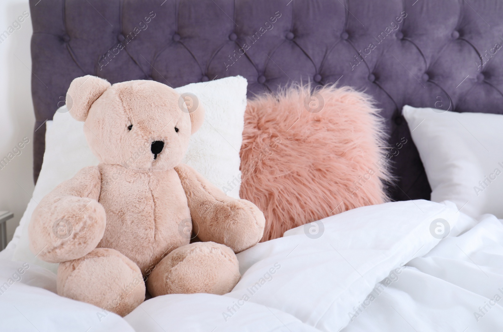 Photo of Cute teddy bear sitting on bed indoors. Space for text