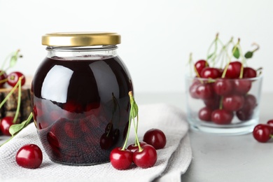 Photo of Jar of pickled cherries and fresh fruits on light table, closeup