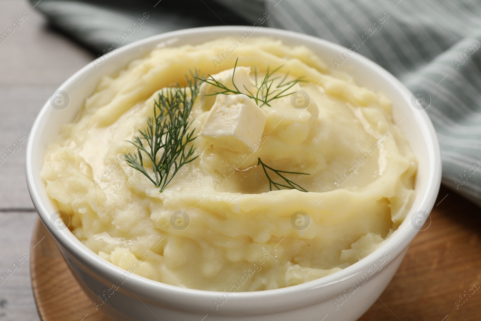 Photo of Bowl of delicious mashed potato with dill and butter on wooden table, closeup