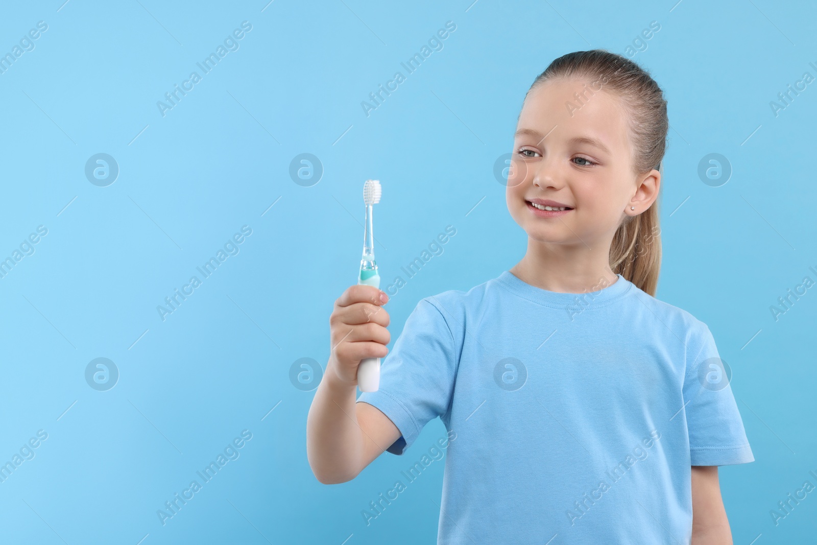 Photo of Happy girl holding electric toothbrush on light blue background. Space for text