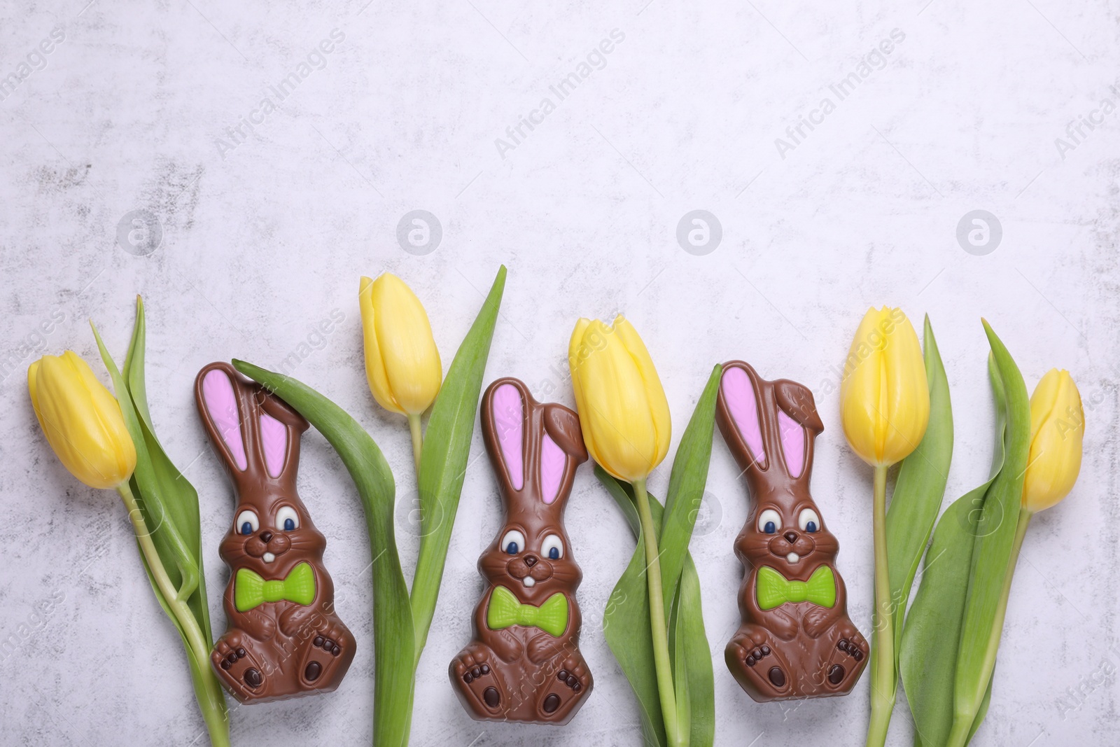 Photo of Flat lay composition with chocolate Easter bunnies and beautiful tulips on white textured table. Space for text