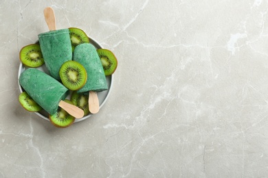 Photo of Plate with delicious spirulina popsicles and kiwi on grey background, top view. Space for text