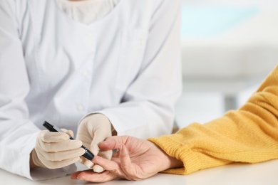 Photo of Doctor taking patient's blood sample with lancet pen in hospital, closeup. Diabetes control