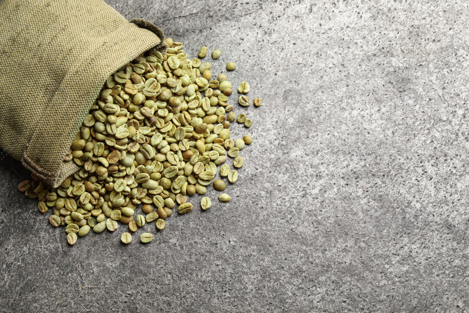 Photo of Overturned sackcloth bag with green coffee beans on grey table, flat lay. Space for text