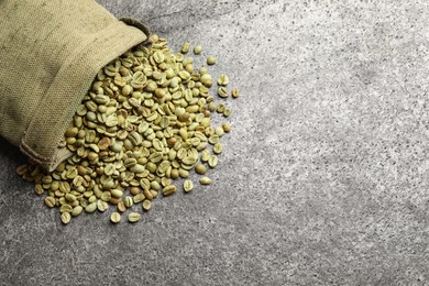 Overturned sackcloth bag with green coffee beans on grey table, flat lay. Space for text