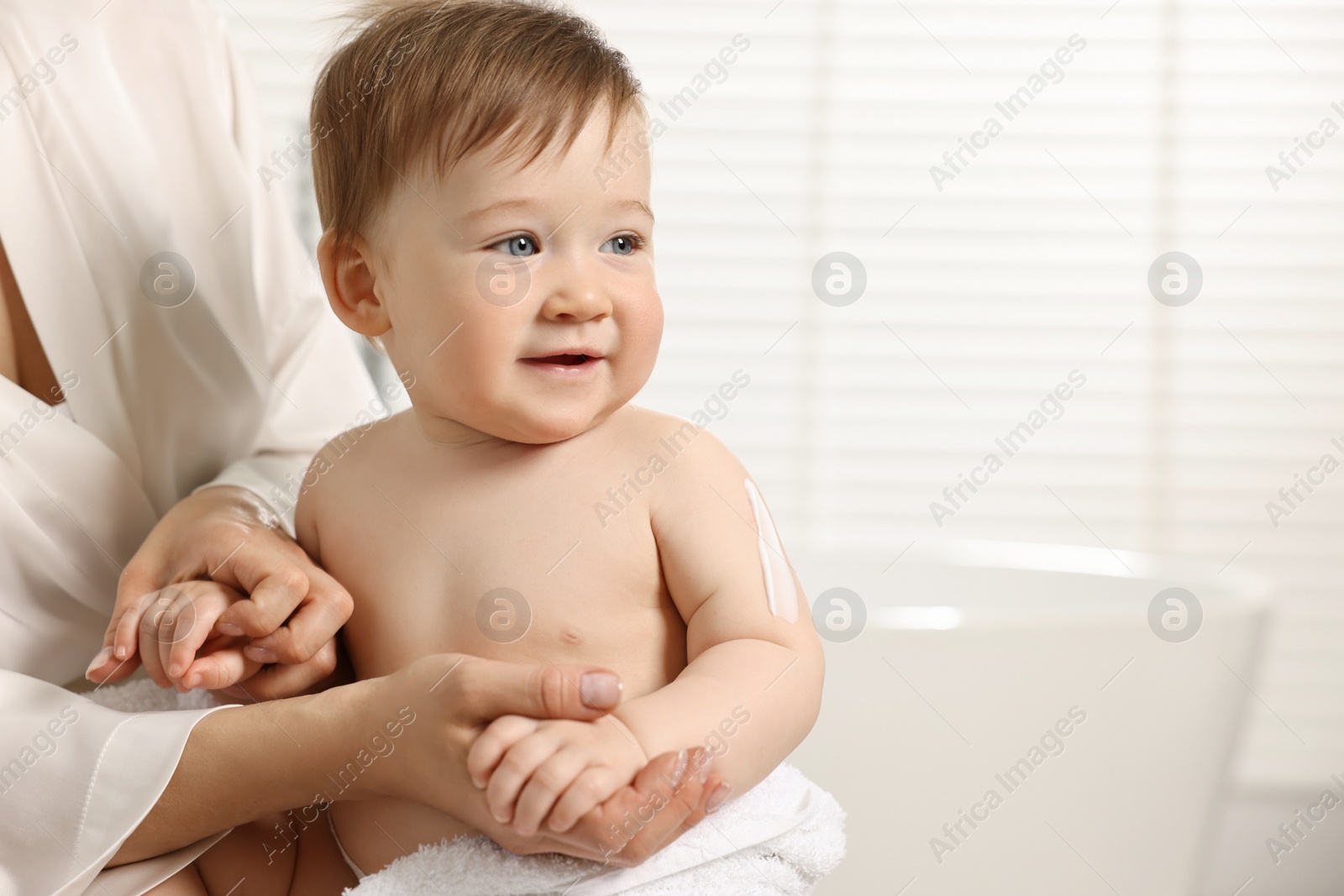 Photo of Mother applying body cream onto baby`s skin indoors, closeup. Space for text