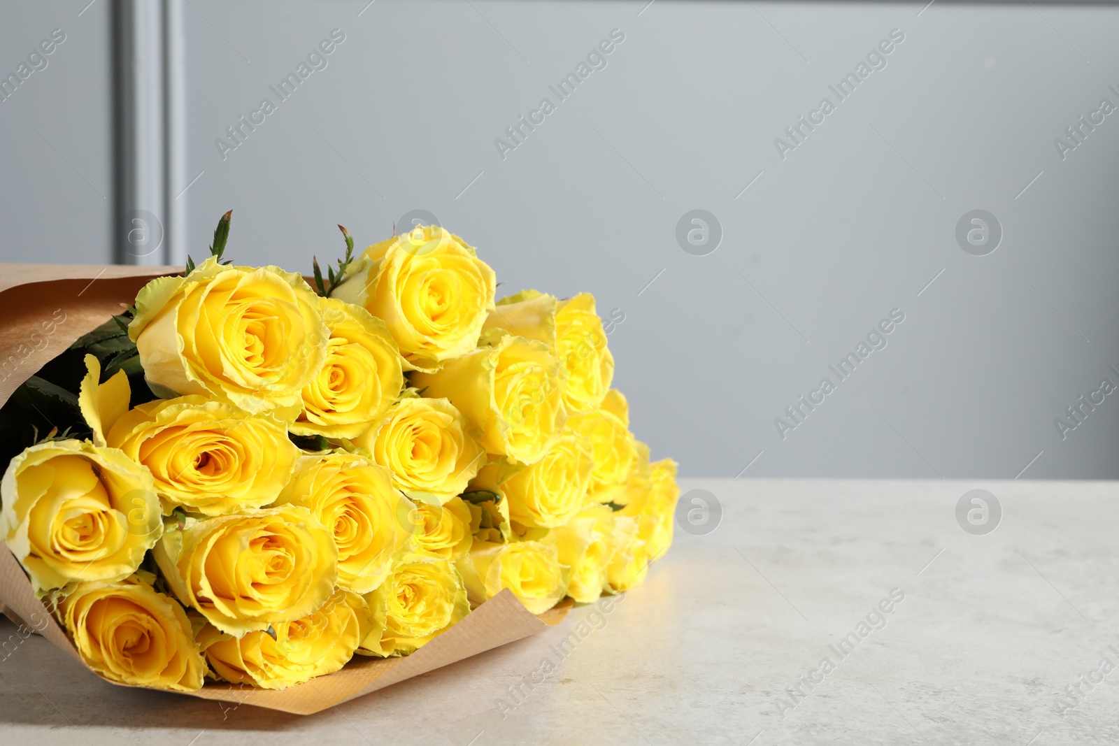 Photo of Beautiful bouquet of yellow roses on light grey table, space for text