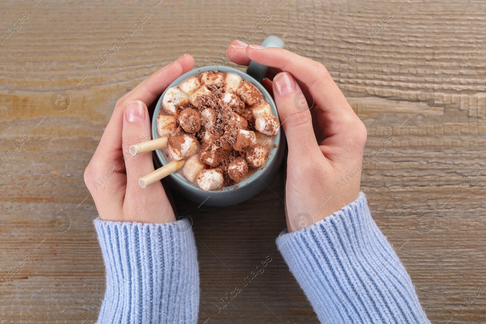 Photo of Woman drinking aromatic hot chocolate with marshmallows and cocoa powder at wooden table, top view