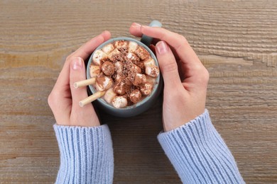 Woman drinking aromatic hot chocolate with marshmallows and cocoa powder at wooden table, top view