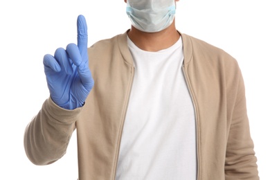 Man in protective face mask and medical gloves with raised index finger on white background, closeup