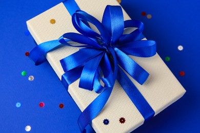 Beautiful gift box with bow and confetti on blue background, closeup