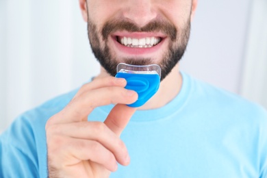 Photo of Young man using teeth whitening device on light background, closeup
