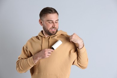 Photo of Young man cleaning clothes with lint roller on grey background