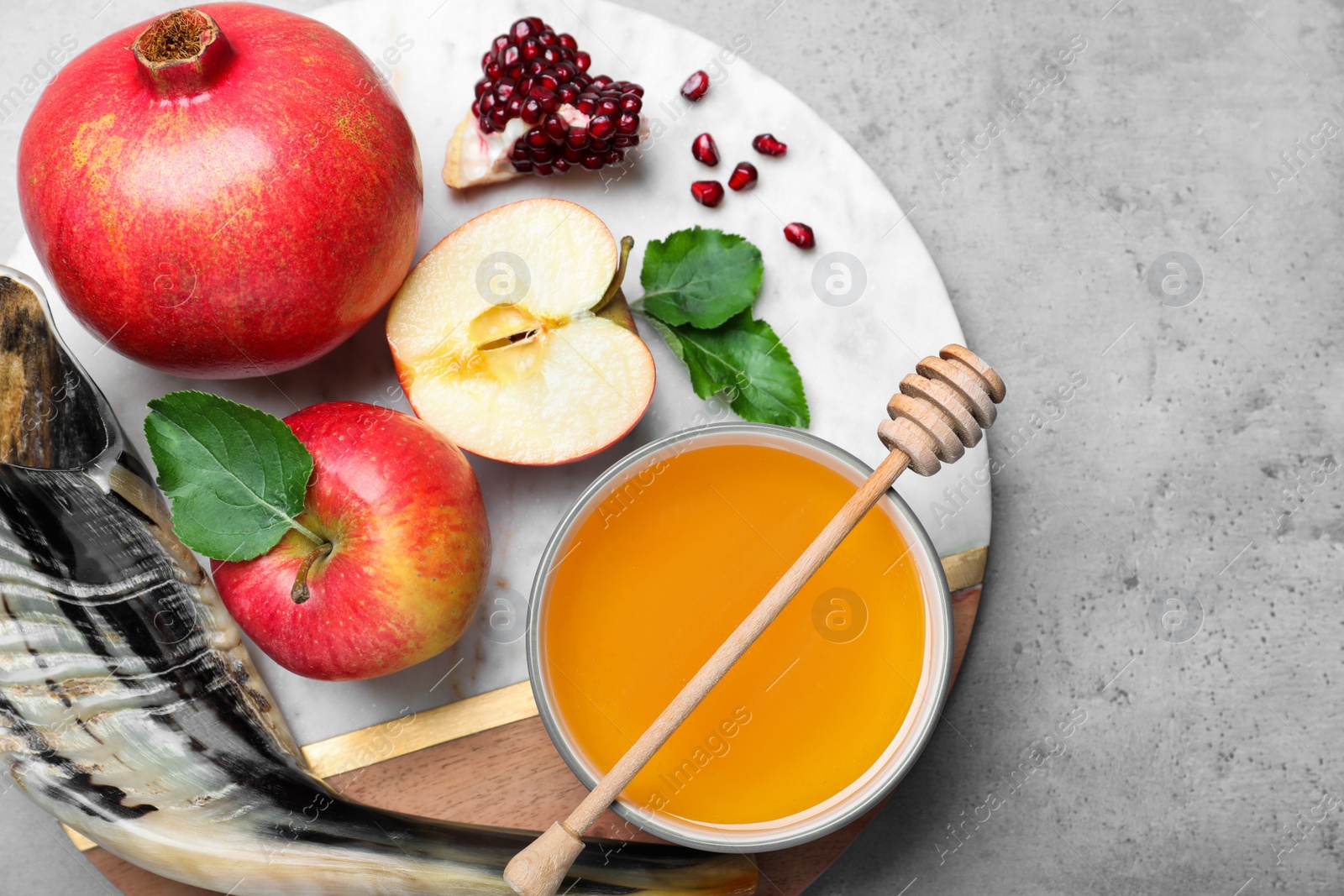 Photo of Honey, pomegranate, apples and shofar on grey table, top view. Rosh Hashana holiday