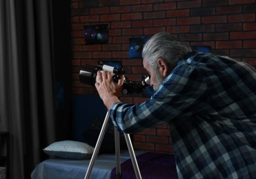 Senior man looking at stars through telescope in room