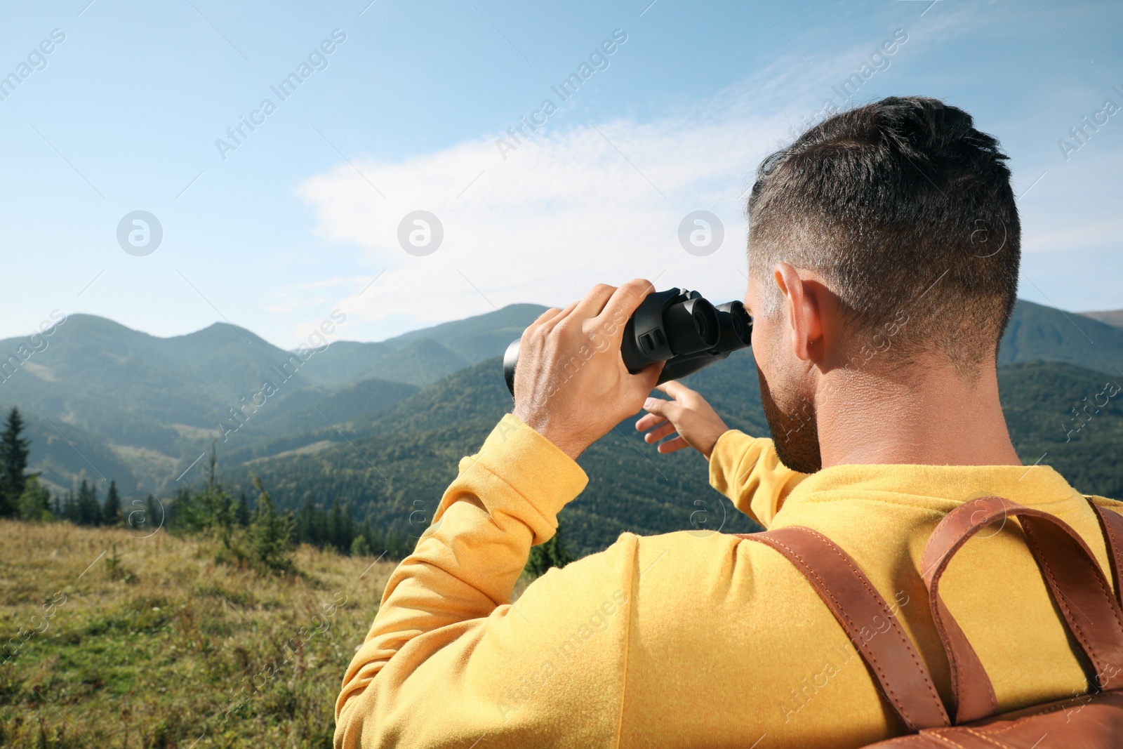 Photo of Man with binoculars in mountains on sunny day, space for text