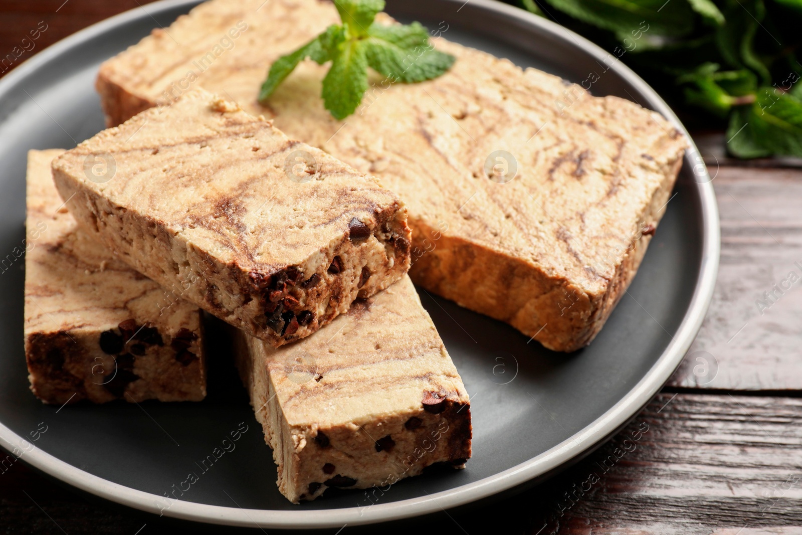 Photo of Pieces of tasty chocolate halva with mint on wooden table, closeup