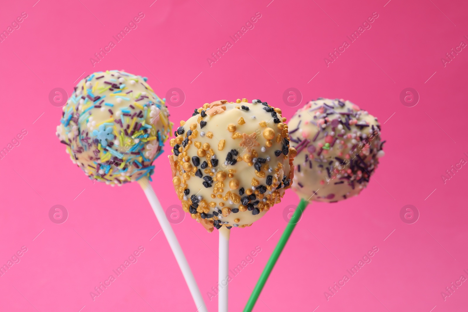 Photo of Sweet cake pops decorated with sprinkles on pink background, closeup. Delicious confectionery
