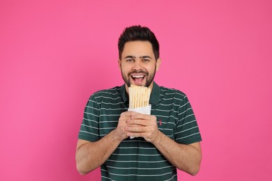 Photo of Young man eating tasty shawarma on pink background