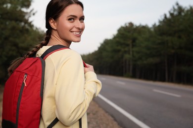 Young woman with backpack on road near forest