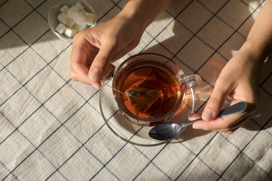 Photo of Woman holding spoon near glass cup with tea bag at table, above view