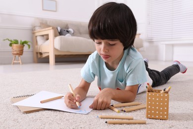Photo of Cute little boy drawing with pencils on floor at home