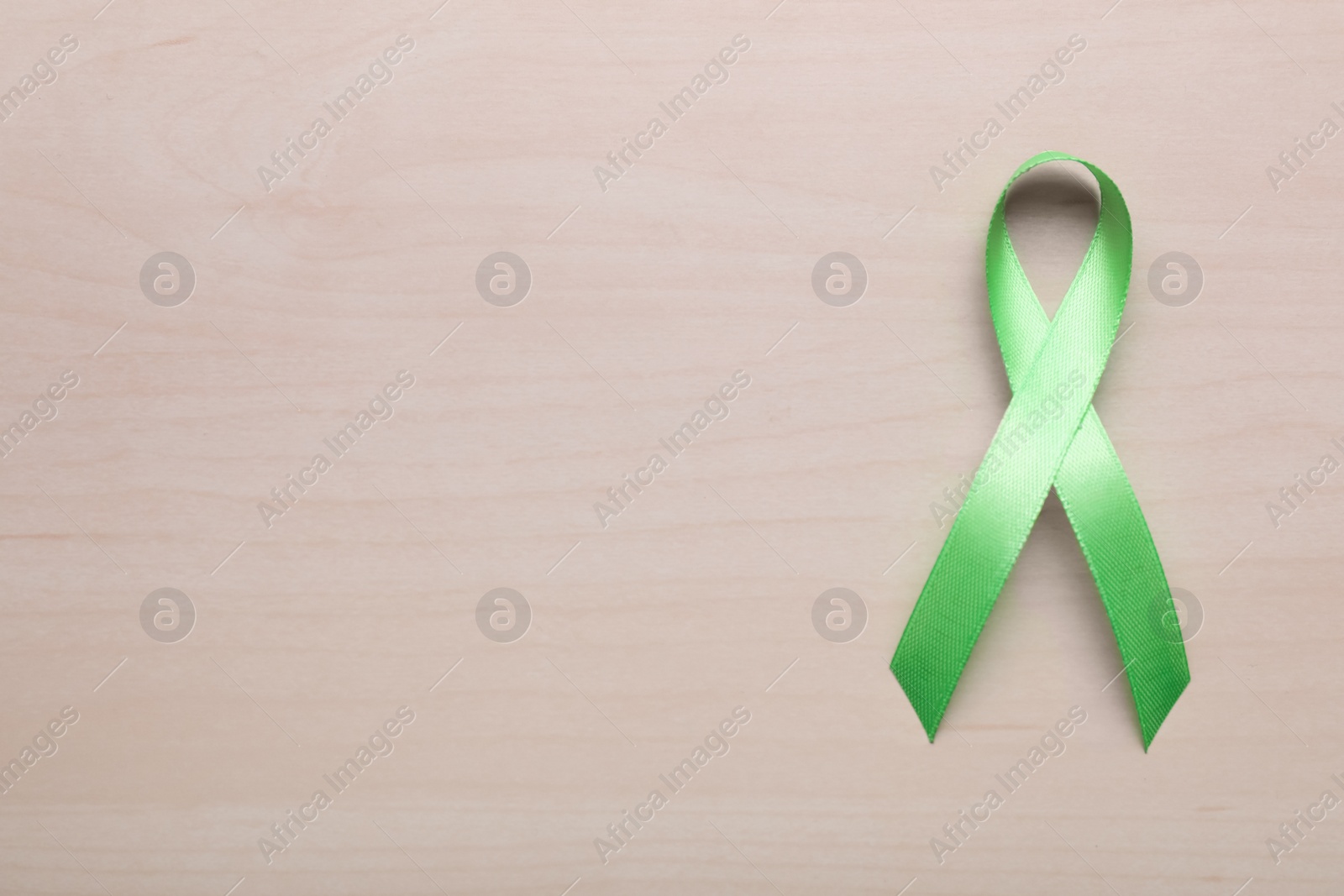 Photo of World Mental Health Day. Green ribbon on wooden background, top view with space for text