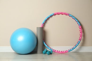 Photo of Hula hoop, exercise ball, yoga mat and dumbbells near beige wall in gym
