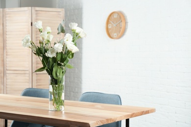 Vase with beautiful flowers as element of interior design on table in room. Space for text