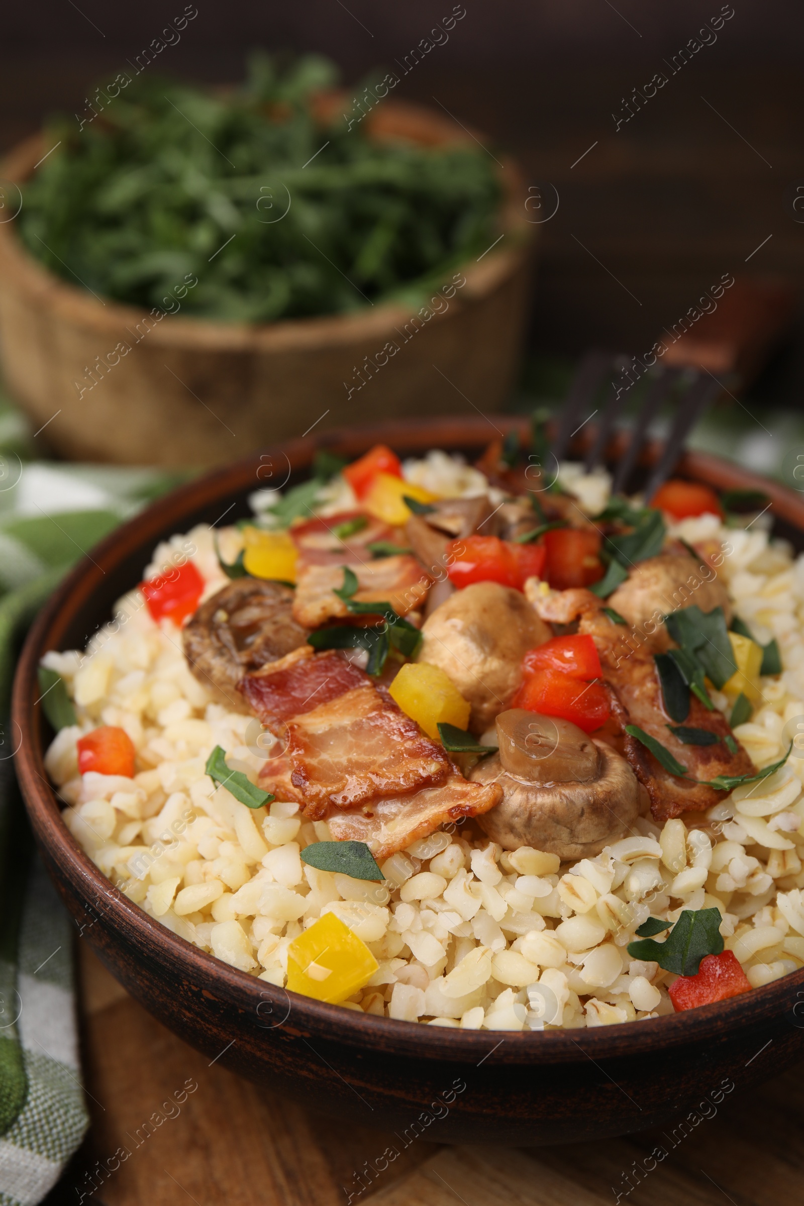 Photo of Cooked bulgur with vegetables, fried bacon and mushrooms in bowl on wooden table, closeup