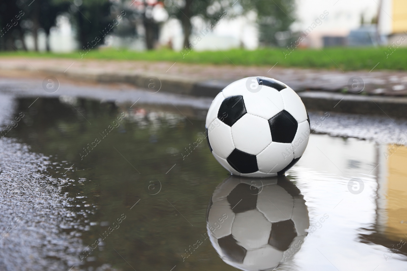 Photo of Soccer ball near puddle outdoors, space for text