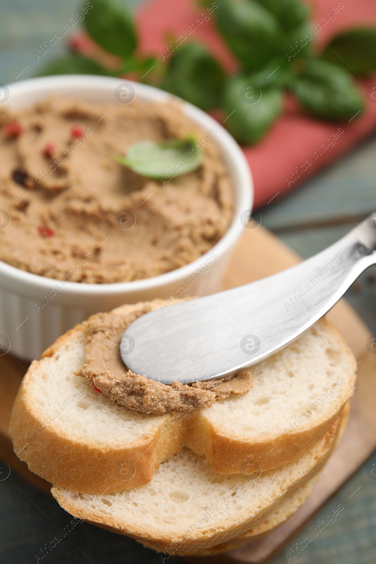 Photo of Spreading delicious meat pate onto slice of bread and knife on table, closeup