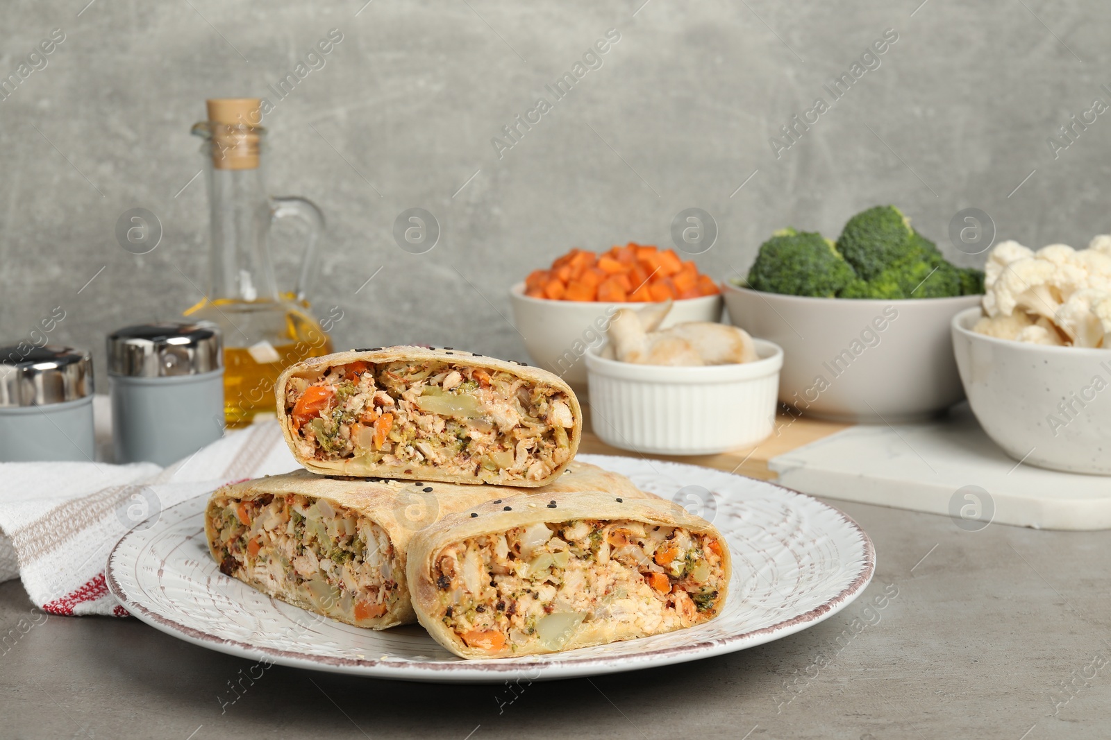 Photo of Pieces of delicious strudel with chicken, vegetables and products on light grey textured table, closeup