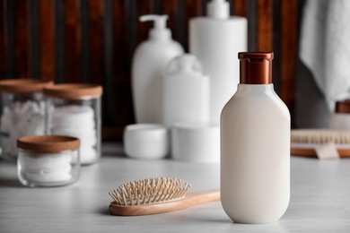 Bottle of shampoo, wooden hairbrush and toiletries on white table indoors, space for text