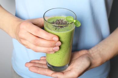 Photo of Woman holding glass of fresh green smoothie with chia seeds on grey background, closeup