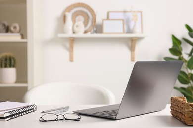 Photo of Home office. Laptop, glasses and stationery on white desk indoors. Space for text