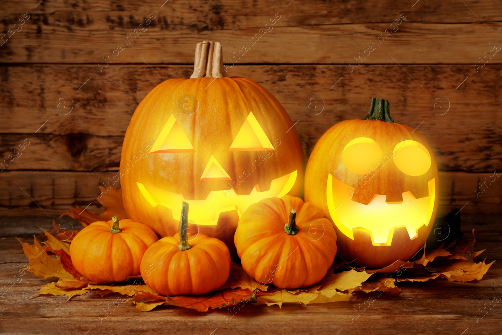 Image of Spooky jack o`lanterns and dry autumn leaves on wooden table. Halloween decor