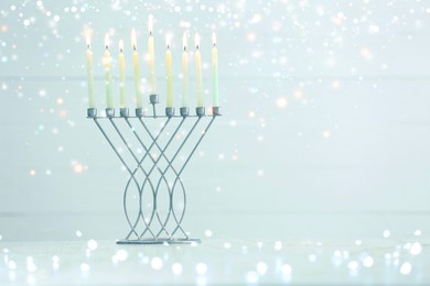 Image of Hanukkah celebration. Menorah with burning candles on table against light background, space for text