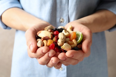 Photo of Young woman holding handful of different dried fruits and nuts, closeup